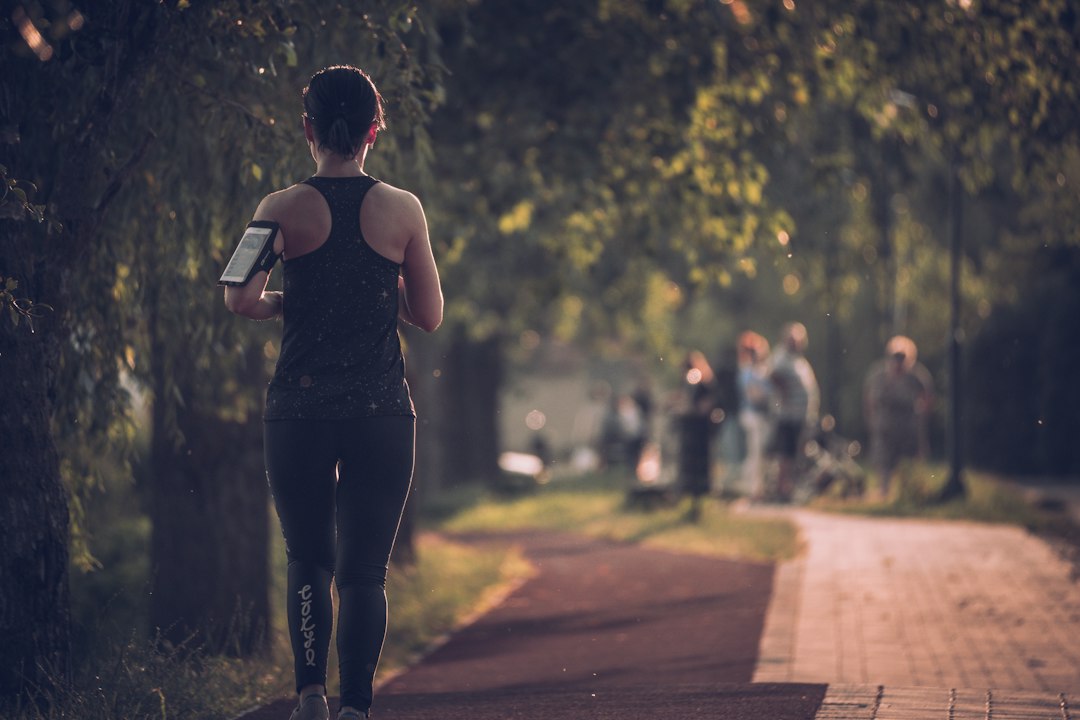 A smiling woman joins a running club group in a London park during autumn, wearing a light jacket and trainers.